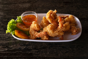 Fried prawns in breadcrumbs with sauce on white plate. seafood on dark background.