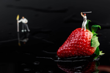 miniature golfer on strawberry on black background 