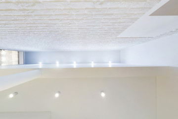 suspended ceiling with led lightspot lamps and drywall construction in empty room in apartment or house. Stretch ceiling white and complex shape. looking up