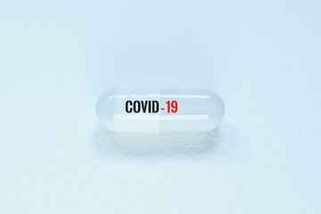 White medicinal capsule on a white background. A text on the capsule says covid-19. Concept of...