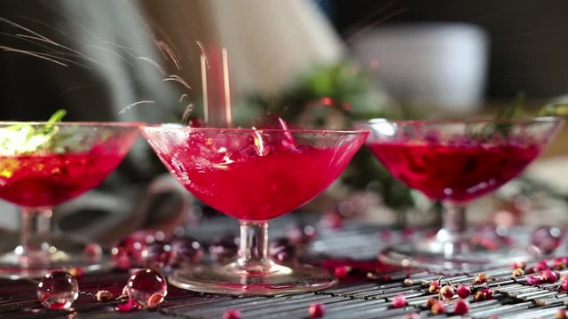 beautiful red cocktail in a martini glass, cocktail with rosemary and rose petals. Ice falls into a glass