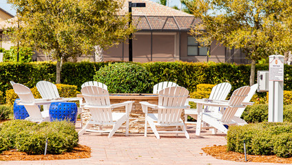 A large fire pit surrounded by white Adirondack chairs