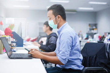 Men infected with Covid Coronavirus sit at the office with other colleagues.