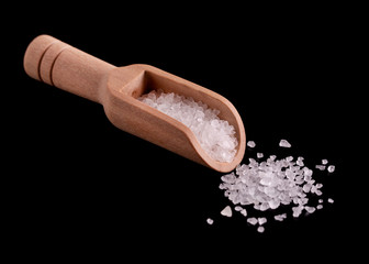 Salt in a wooden spoon. Large crystals of white salt in a wooden spoon. Scattered salt crystals on a black background.