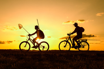 Fototapeta na wymiar Father and son returning from fishing in the evening, silhouettes of people riding bicycles in nature 