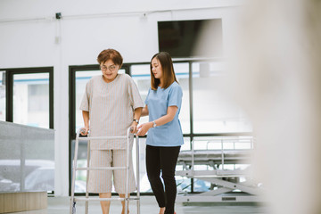 young physical therapist helping senior patient in using walker during rehabilitation