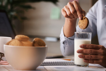 Close-up of businesswoman dipping cookie in glass of milk.