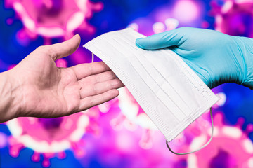 Doctor's hand in a blue gloved glove hands a medical mask to a patient's hand