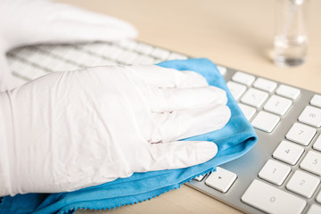 Hand with gloves cleaning a keyboard with disinfectant. COVID-19 Coronavirus outbreak contamination...