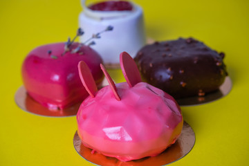 Mini mousse pastry dessert covered with mirror glaze on yellow background. Modern european cake. French cuisine.