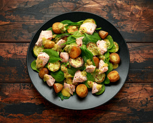 Salmon, new potato, courgette and spinach salad on wooden table