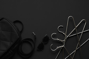 Accessories for women's beauty. Black monochromatic composition on black background. Hangers, belt, handbag.Minimalist black, black friday.Top view, Copy Space Flat Lay.