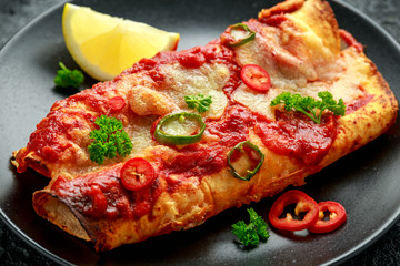 Baked Chicken fillets enchiladas with courgette, salsa sauce and cheese served with lemon wedges and chilies