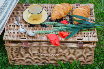 Wicker picnic basket on grass with food and coffee