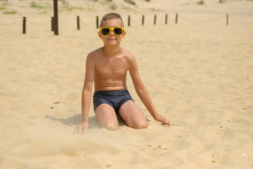 Little boy in sunglasses on the beach. Child in swimming trunks on the sea sand.