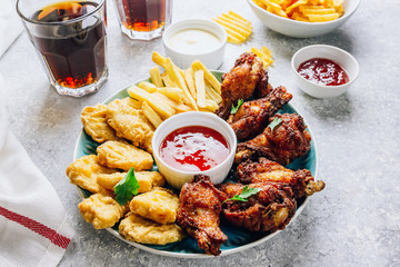 Table fof tasty snacks for beer prepared for watching sports on TV. Chicken. Chicken wings, chicken nuggets, french fries, chips, various sauces and lemonade. Light gray background. Selective focus