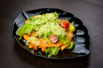 Caesar salad with chicken on a black plate on wooden table