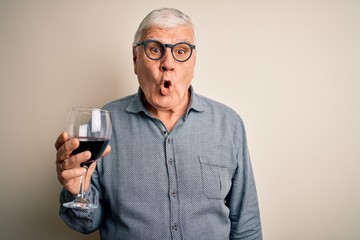 Senior handsome hoary man drinking glass of red wine over isolated white background scared in shock with a surprise face, afraid and excited with fear expression