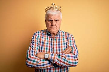 Senior handsome hoary man wearing golden crown of king over isolated yellow background skeptic and nervous, disapproving expression on face with crossed arms. Negative person.