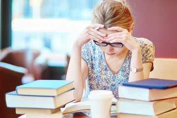 Exhausted student with books and papers, studying at home