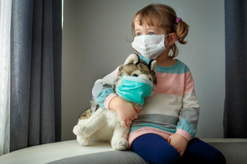 Quarantine at kindergarten. Toddler girl and her dog toy with protection masks. Coronavirus...