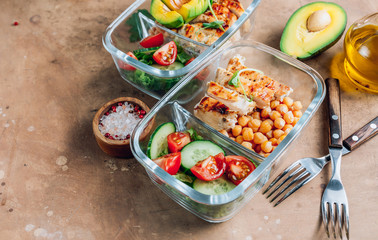 Healthy meal prep containers with chickpeas, chicken, tomatoes, cucumbers and avocados. Healthy lunch in glass containers on beige rustic background. Zero waste concept. Selective focus.