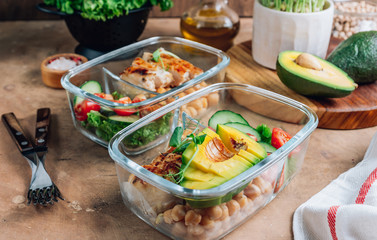 Healthy meal prep containers with chickpeas, chicken, tomatoes, cucumbers and avocados. Healthy lunch in glass containers on beige rustic background. Zero waste concept. Selective focus.
