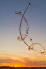 Akrobacje samolotowe na niebie podczas zachodu słońca. Zespół akrobacyjny podczas pokazów lotniczych wykonujący podniebne ewolucje. - obrazy, fototapety, plakaty