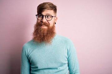 Handsome Irish redhead man with beard wearing glasses over pink isolated background smiling looking to the side and staring away thinking.