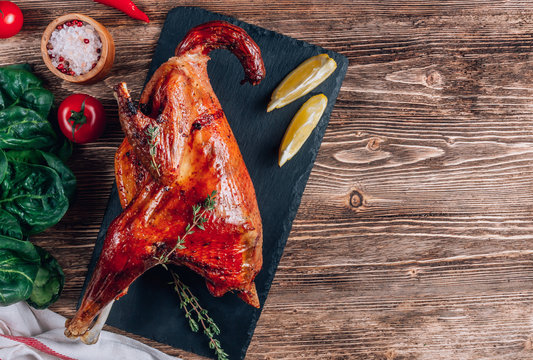 Roasted rooster with spices, lemon and thyme on black dish on rustic wooden background. Healthy food. Top view. Copy space
