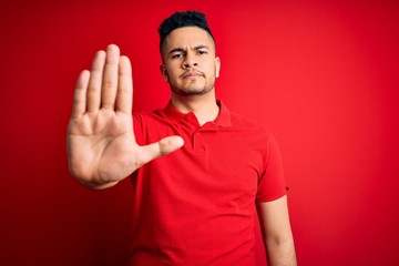 Young handsome man wearing red casual polo standing over isolated background doing stop sing with...
