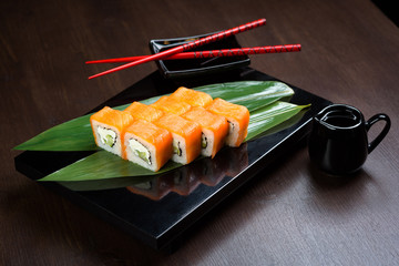 Rolls with salmon and cheese on the board with sauce and red chopsticks