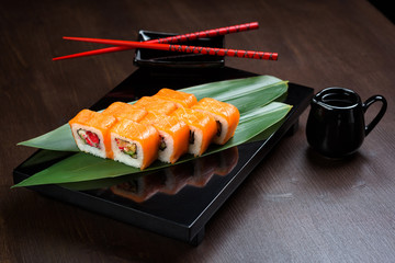 Rolls with salmon and tobiko on the board with sauce and red chopsticks