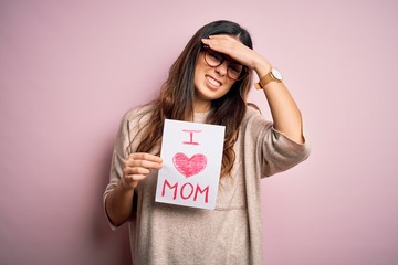 Young beautiful woman holding paper with love mom message celebrating mothers day stressed with hand on head, shocked with shame and surprise face, angry and frustrated. Fear and upset for mistake.