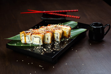 Rolls with eel and cheese on the board with sauce and red chopsticks