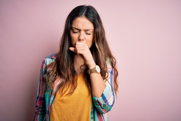 Young beautiful brunette woman wearing casual colorful shirt standing over pink background feeling...