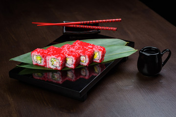 Rolls with tobiko and avocado on the board with sauce and red chopsticks