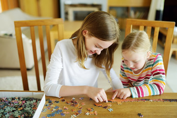 Cute young girls playing puzzles at home. Children connecting jigsaw puzzle pieces in a living room...