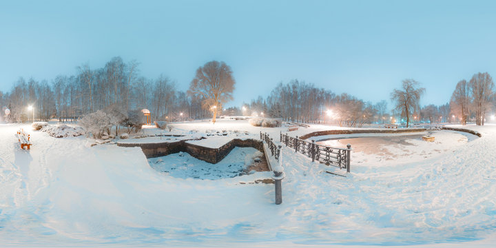 Image with 3D spherical panorama with 360 degree viewing angle. Snowy winter in park with trees at the evening. Burning lanterns. Lake Ready for virtual reality in vr. Full equirectangular projection.