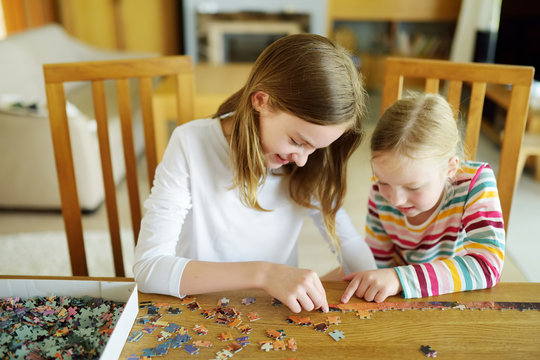Cute young girls playing puzzles at home. Children connecting jigsaw puzzle pieces in a living room table. Kids assembling a jigsaw puzzle. Fun family leisure.