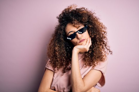 Young beautiful woman with curly hair and piercing wearing funny thug life sunglasses thinking looking tired and bored with depression problems with crossed arms.