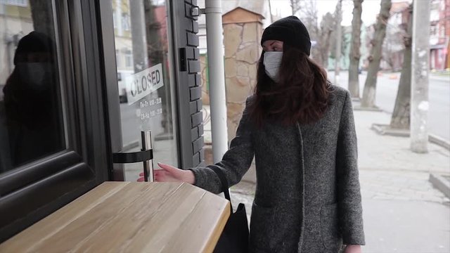 Woman walking wearing medical mask against coronavirus. She is touching the closed doors of a cafe and walks by
