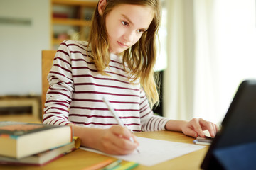 Smart preteen schoolgirl doing her homework with digital tablet at home. Education and distance learning for kids. Homeschooling during quarantine.