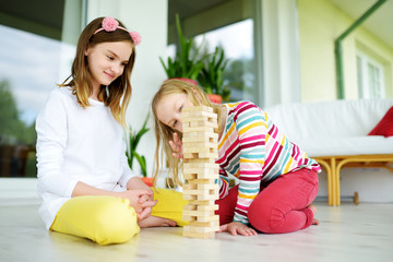 Two sisters playing wood blocks tower game at home. Kids practicing their physical and mental skills. Fun board games for family leisure. Stay at home activity for kids.