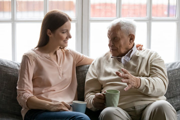 Talk during teatime with aged man, caregiver listens life memories stories of old 75s patient seated on sofa in cozy living room. Provide support care and attention of older generation people concept