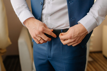 A man, groom buttoned a black leather trouser belt. Groom dress up a belt with buckle. Businessman wear leather stylish belt.