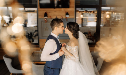 Fototapeta premium Newlywed bride and groom touch their eyes with their eyes closed and hold hands. Beautiful elegant couple of newlyweds in love in a loft interior. Wedding concept. Happy newlywed couple.