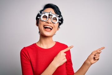 Young beautiful asian girl wearing optometry glasses standing over isolated white background smiling and looking at the camera pointing with two hands and fingers to the side.