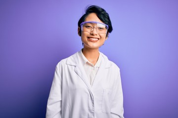 Young beautiful asian scientist girl wearing coat and glasses over purple background with a happy...