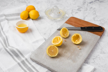 Whole and Cut Lemons on Cement Cutting Board on White Marble Counter; Lemon Juicer Nearby with Cup of Lemon Juice